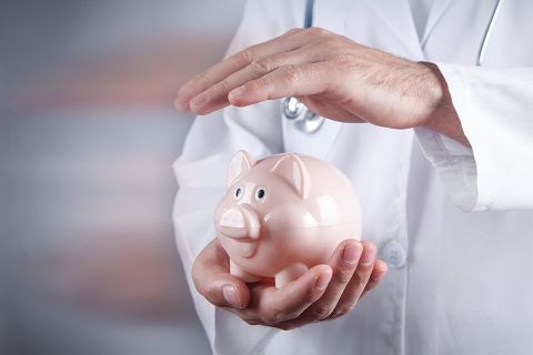 Arzt hält Hand über Sparschwein